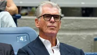 ABD Açık Tenis Turnuvası'nda kort saati 0.07'yi gösterirken kameraya yansıyan ve gülümseyen Pierce Brosnan.